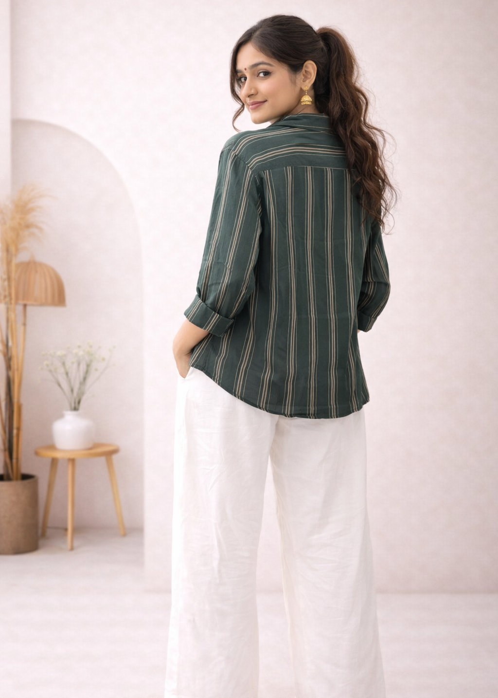 Woman wearing a green striped shirt and white pants in a minimalistic room.